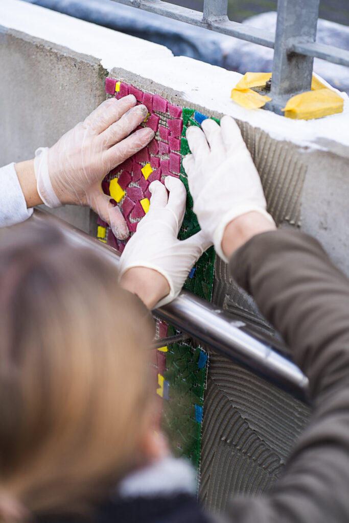 Mosaikteile auf Netz werden in den Zement gedrückt